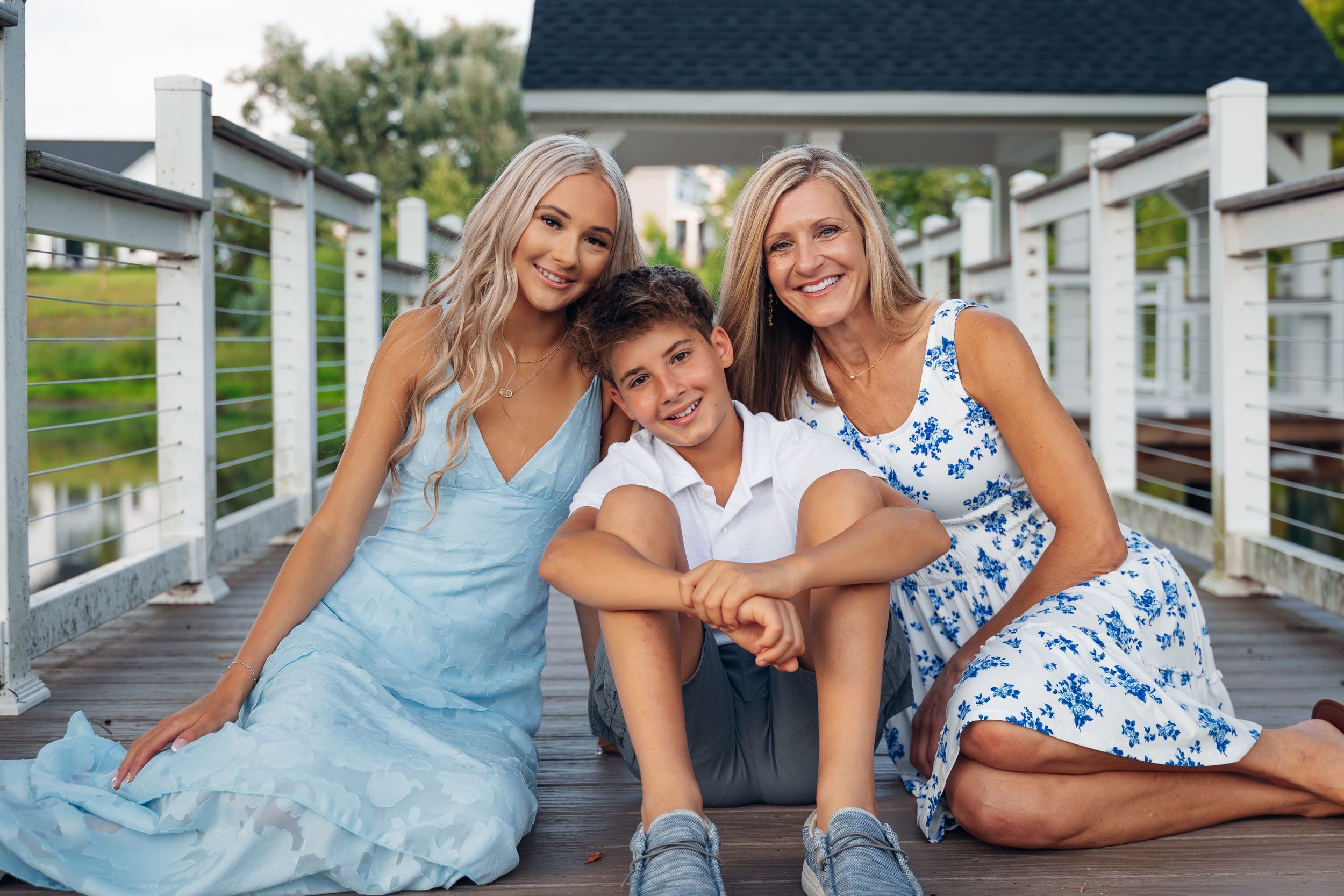 Family portrait of two blonde women and a boy sitting together on a wooden dock, smiling outdoors.