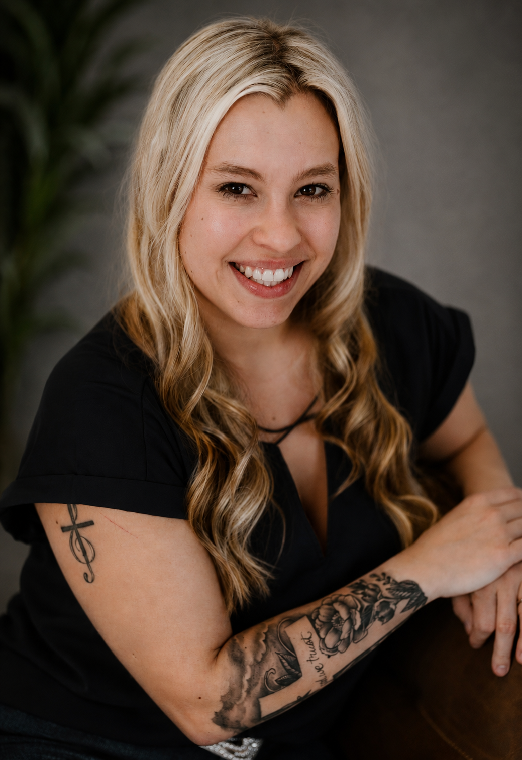 Smiling blonde woman with tattoos wearing a black top, professional headshot portrait.