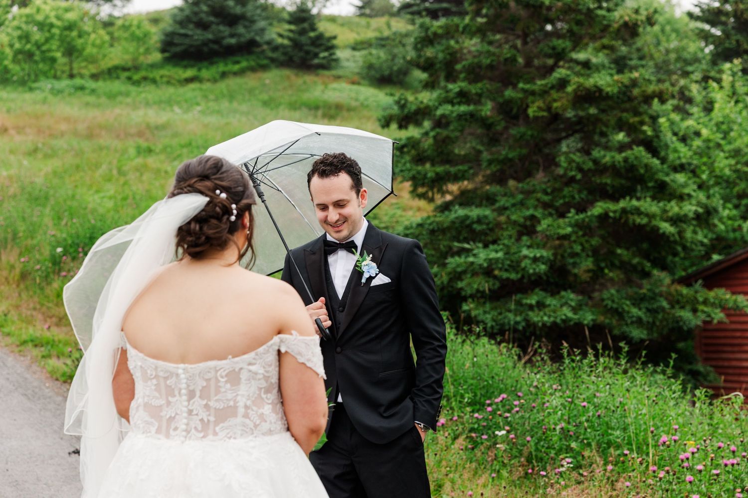 Bride and groom share a romantic first look outdoors, sheltered under a clear umbrella on their rainy wedding day.