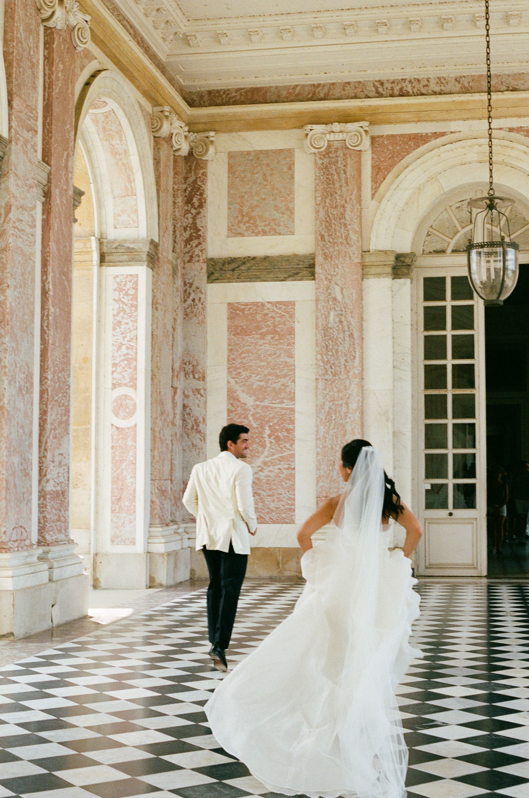 Bride and groom walking through grand marble hall at Le Grand Trianon with checkered floors. Running wedding photos. Versailles wedding