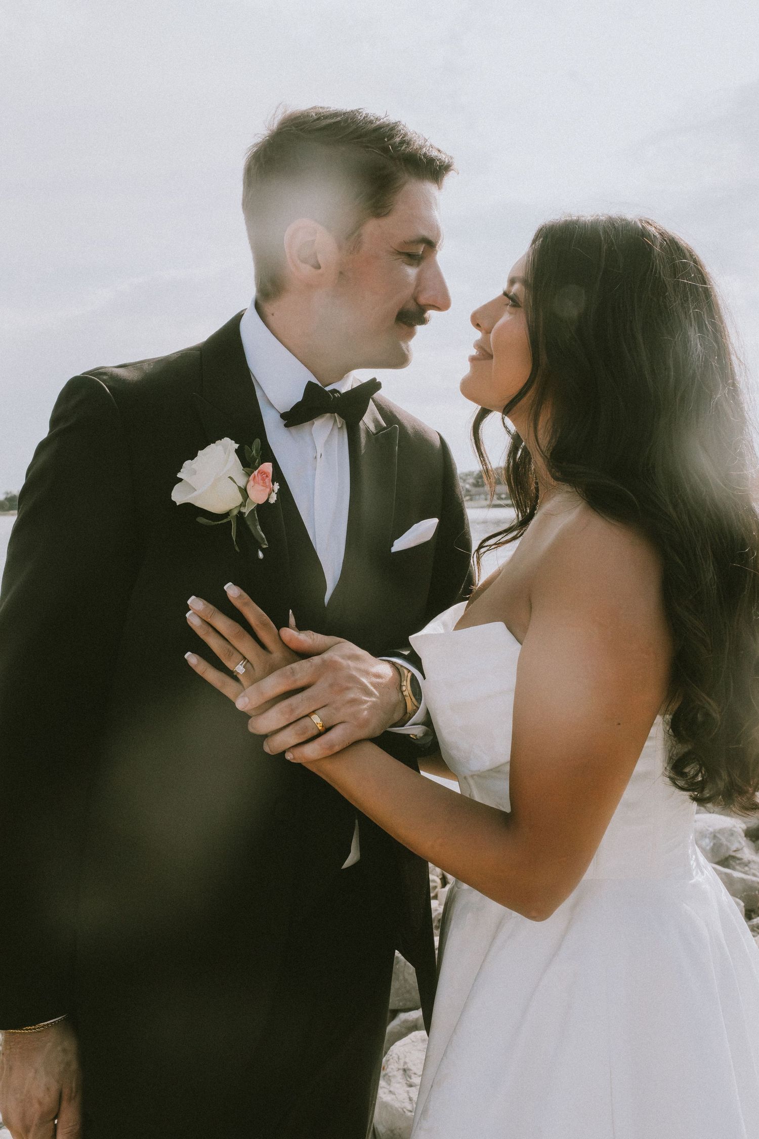 A bride and groom share a romantic moment in wedding attire, with the groom in a black tuxedo and bride in a white strapless gown.