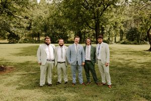 Groom and four groomsmen in coordinating gray suits pose together on a green lawn at outdoor wedding.