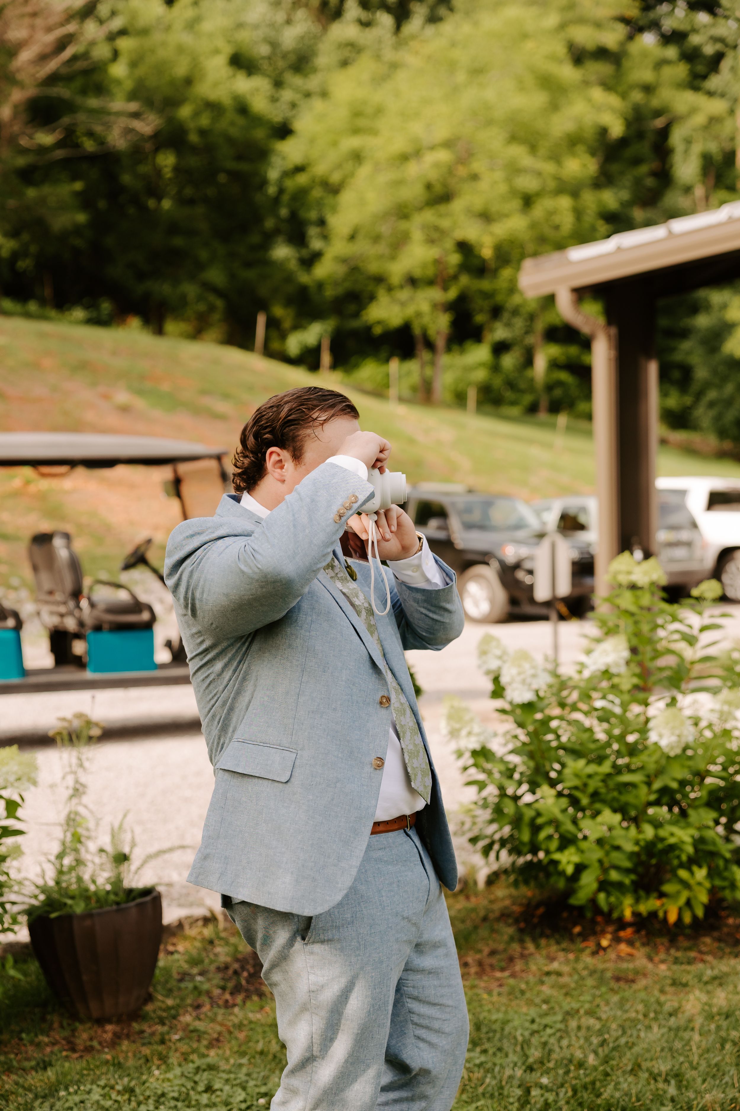 Groom in light blue suit adjusting his tie outdoors before the wedding ceremony on a sunny day.