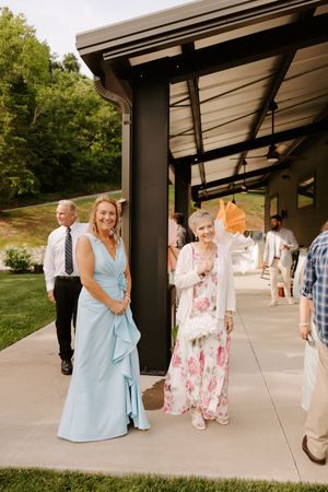 Woman in light blue gown and elderly woman in floral dress smiling at outdoor wedding reception.