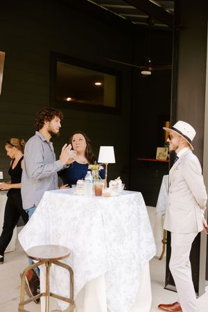 Three people converse around a white tablecloth table at an elegant indoor event venue.