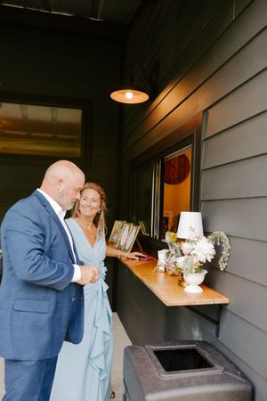 A bald man in a blue suit and a woman in a light blue dress review items at a wedding venue counter.