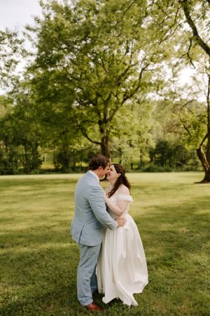 Bride and groom share a romantic almost-kiss while embracing in a lush green park during their outdoor wedding.