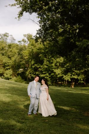 Bride and groom walking hand in hand on lush green hillside at golden hour.