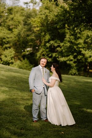 Bride and groom share romantic moment on green hillside, bride touching groom's chest in golden light.
