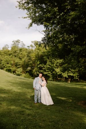 Bride and groom posing together on a lush green hillside surrounded by trees on their wedding day.