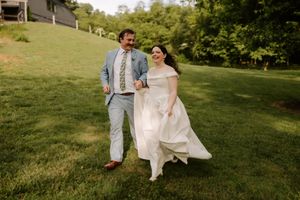 A joyful bride and groom run hand-in-hand across a lush green lawn on their wedding day.
