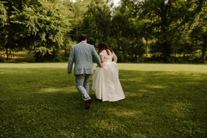 Bride and groom walking hand in hand across a green lawn surrounded by trees after their wedding.