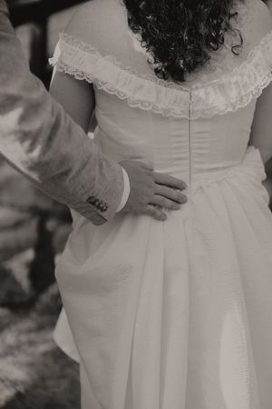 Black and white close-up of groom placing hand on bride's waist showing back of wedding gown.