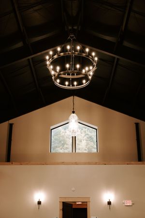Rustic wedding venue interior featuring a wrought iron chandelier beneath a vaulted dark wood ceiling.