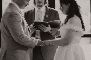 Bride and groom exchange vows with officiant during intimate black and white wedding ceremony.