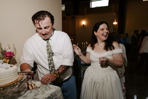 Bride and groom laugh joyfully while cutting their wedding cake at indoor reception.