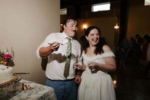 Laughing bride and groom enjoy wedding cake tasting moment together at reception celebration.