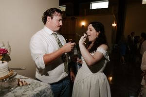 Bride and groom sharing wedding cake at their reception in a warmly lit venue.
