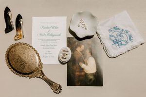 Wedding flat lay with invitation, rings, vintage mirror, bridal handkerchief, and classic painting.