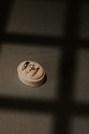 Three gold wedding rings displayed in a velvet ring box with dramatic window shadow light on dark background.