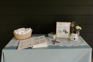 Wedding guest book table with Polaroid camera, photo album, basket of cards, and floral arrangement.