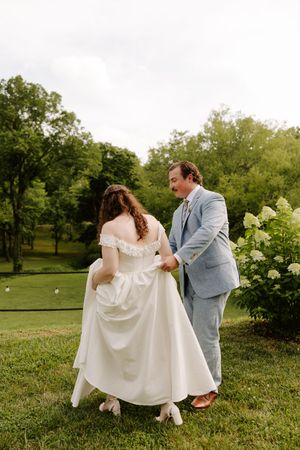 Bride and groom walking hand-in-hand on lush green lawn near blooming hydrangeas during outdoor wedding.