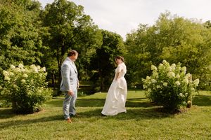 Bride and groom share a joyful first look moment surrounded by blooming white hydrangea bushes outdoors.