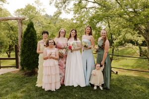 Bride with bridesmaids in pink and sage green dresses with flower girl at outdoor wedding.