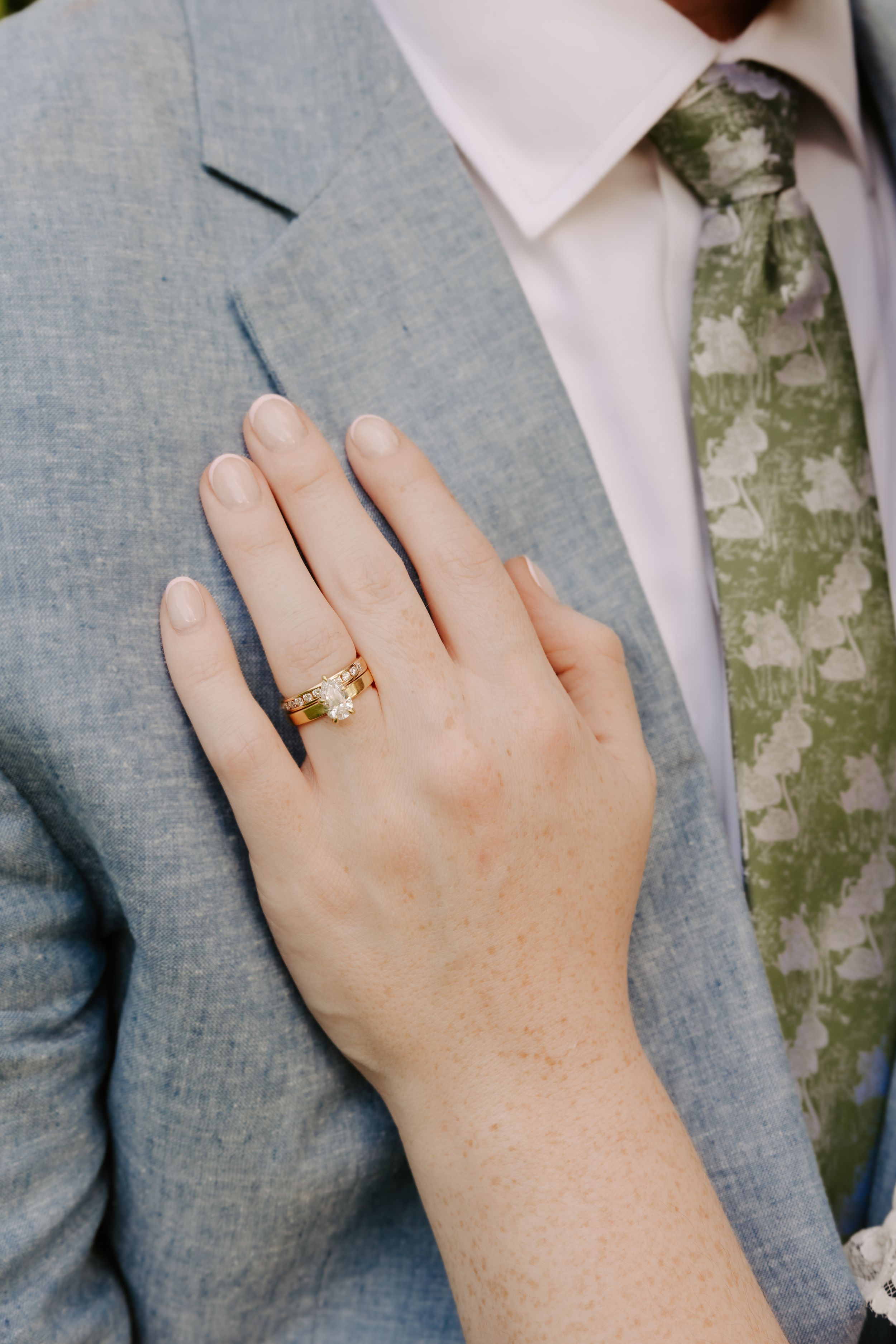 Close-up of bride's hand displaying a gold wedding ring resting on groom's light blue suit jacket.