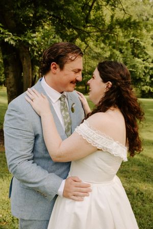 Bride and groom in wedding attire laugh together while embracing in a lush green park setting.