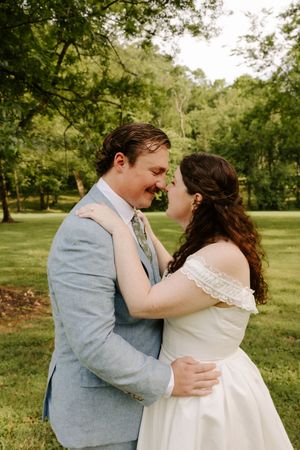 Bride and groom sharing an intimate nose-to-nose moment while embracing in a lush green garden.