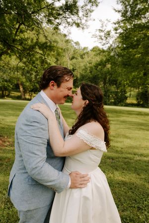 Bride and groom share a romantic almost-kiss moment in a lush green outdoor wedding setting.