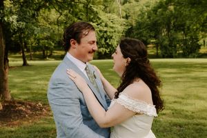 Bride and groom gazing at each other lovingly outdoors, bride in white off-shoulder dress, groom in light blue suit.