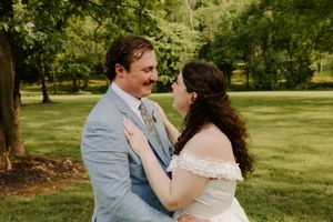 A newlywed couple shares a romantic moment gazing into each other's eyes in a sunlit green park setting.