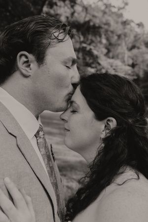 Black and white close-up of a groom tenderly kissing his bride on the forehead during their wedding day.