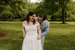 Bride and groom share a joyful moment laughing together on lush green lawn.