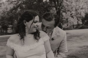 A black and white romantic portrait of a groom whispering to his bride during their outdoor wedding.