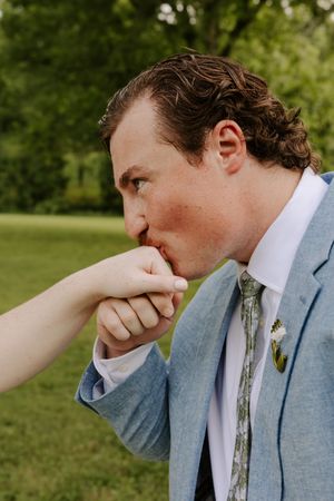 Groom in light blue suit gallantly kisses bride's hand during outdoor wedding portrait session.