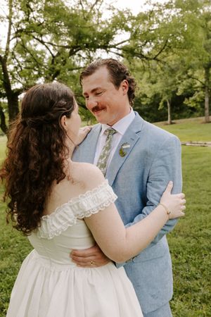 Bride and groom share a tender embrace in green park setting during wedding photo session.