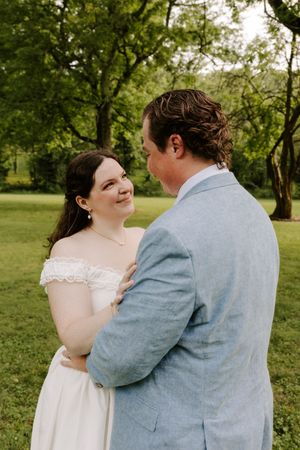 Radiant bride in off-shoulder white gown smiles lovingly at groom during outdoor wedding portraits.