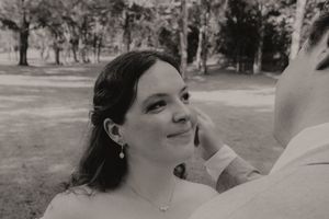 Black and white close-up portrait of a smiling bride as groom gently touches her face outdoors.