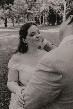 Black and white photo of bride in off-shoulder lace gown gazing up at groom in outdoor setting.