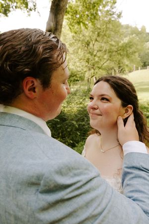 Groom tenderly touches brides face as she smiles up at him during outdoor wedding portrait session.