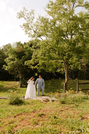 Bride and groom walk hand-in-hand through a sunny garden path on their wedding day.