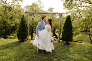 Joyful bride and groom walking and laughing together under a rustic wooden arch in a lush green garden.