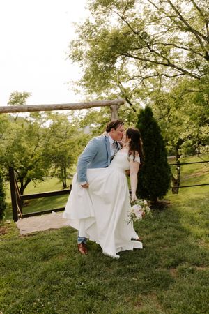 Groom dips bride for a romantic kiss near rustic wooden fence at outdoor garden wedding.