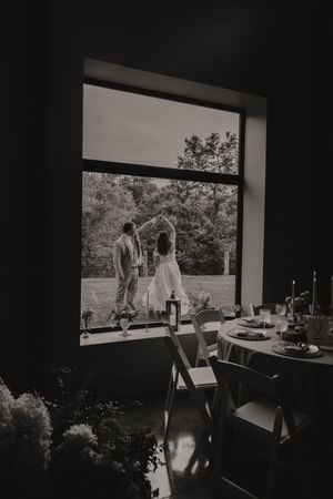Black and white photo of couple dancing outside viewed through venue window.
