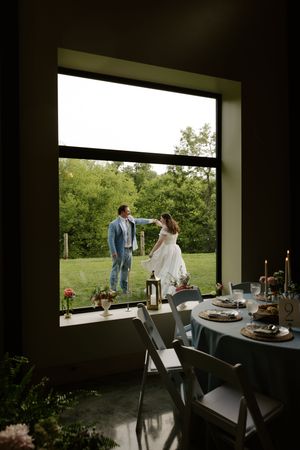 Couple shares romantic dance outside viewed through large window beside candlelit wedding reception table.