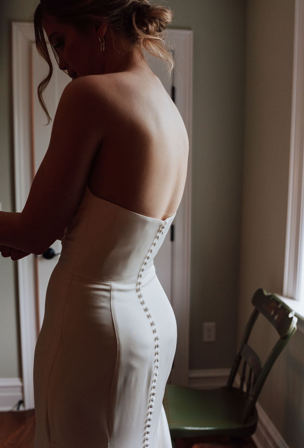Bride in a sleeveless white wedding gown with button detail, showing elegant open back design.