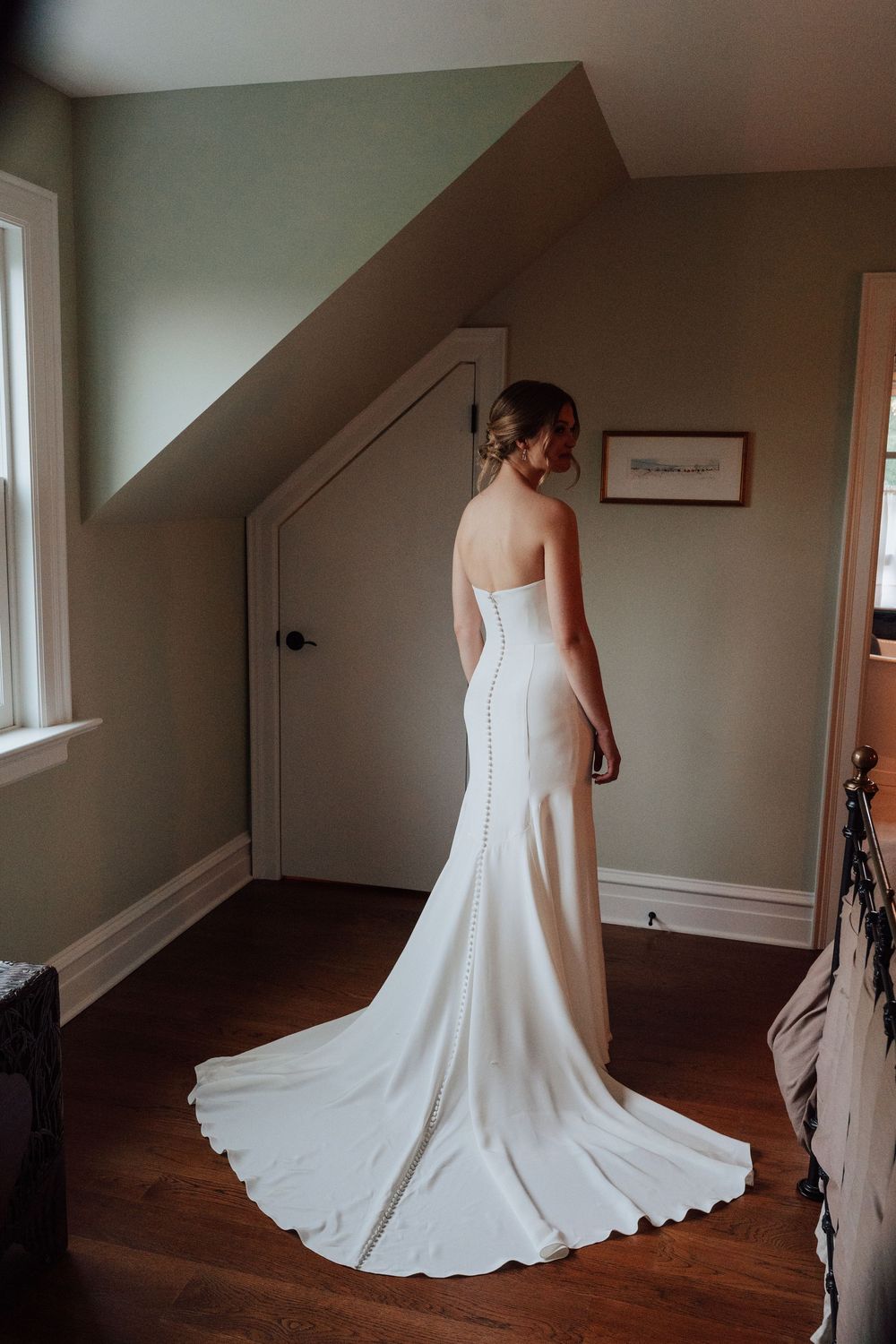 Bride in elegant strapless white wedding gown with train standing in a room with hardwood floors.